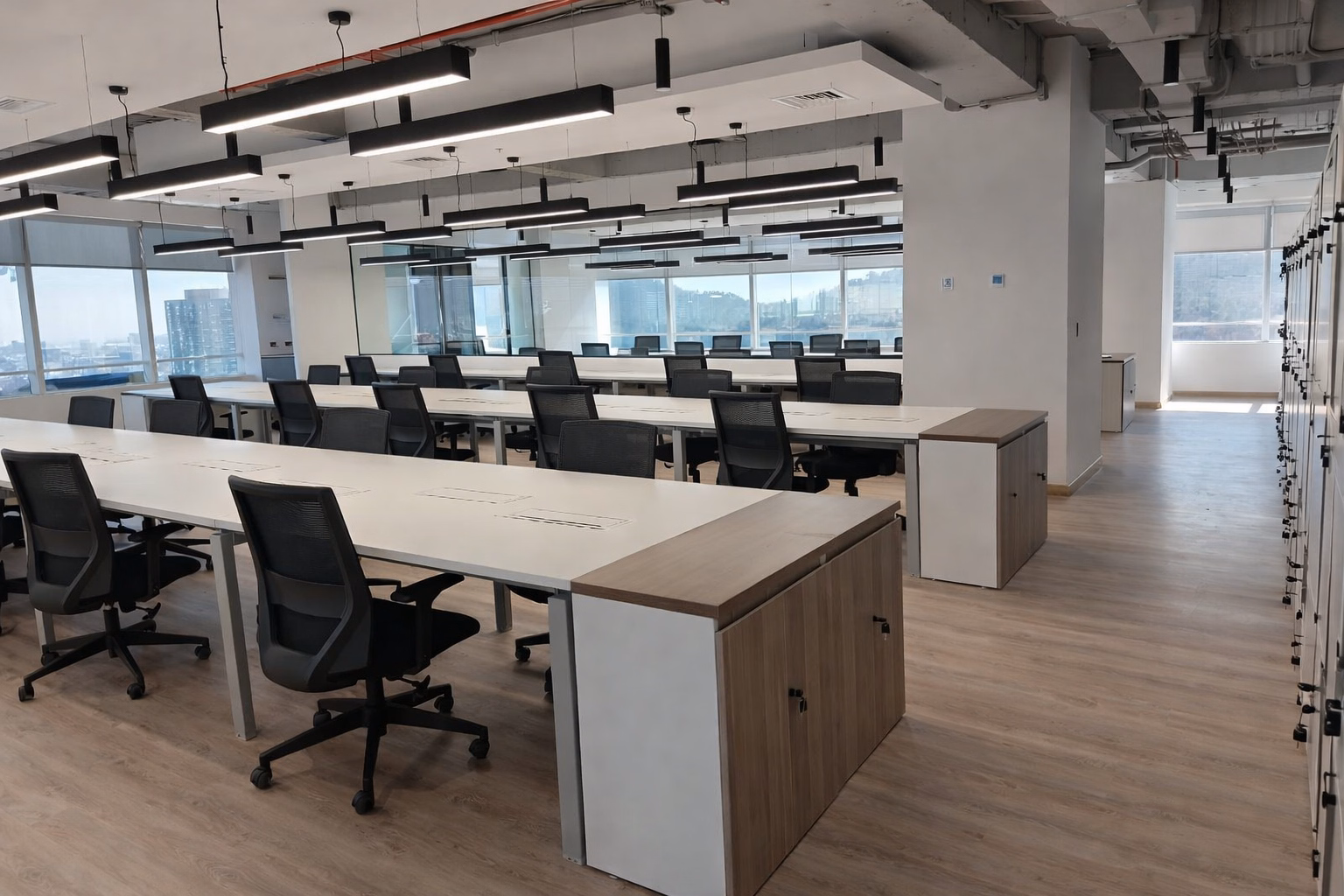 Open space de Oficina Millenium con estaciones de trabajo blancas, cajoneras de madera y ventanales hacia Las Condes